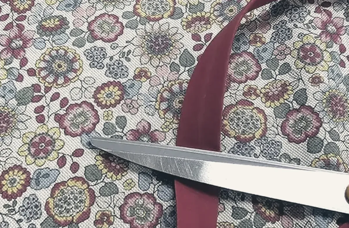 Ciseaux de couture, ruban et fil posés sur un tissu fleuri, dans l'atelier de la boutique